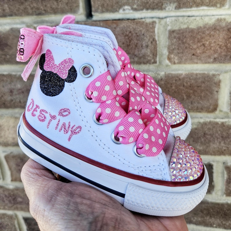 Puede incluir: Zapatillas blancas de ca&ntilde;a alta con cordones de cinta rosa con lunares blancos. Las zapatillas tienen un dise&ntilde;o de Minnie Mouse rosa brillante y el nombre "Destiny" escrito en purpurina rosa en el lateral.