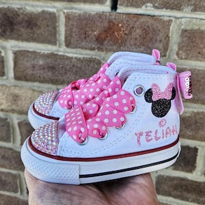 Puede incluir: Zapatillas blancas de ca&ntilde;a alta con cordones de cinta de lunares rosas, un dise&ntilde;o de Minnie Mouse con purpurina rosa y el nombre "YELIAN" en purpurina rosa en el lateral.