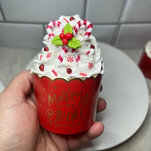 Pode incluir: Um forro de cupcake vermelho com cobertura branca e bast&otilde;es de caramelo vermelho e branco. O forro tem as palavras "Merry & Bright" impressas.