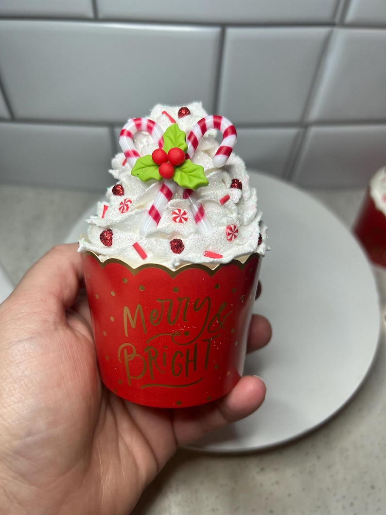 Pode incluir: Um forro de cupcake vermelho com cobertura branca e bast&otilde;es de caramelo vermelho e branco. O forro tem as palavras "Merry & Bright" impressas.
