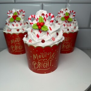 Pode incluir: Tr&ecirc;s forros de cupcake vermelhos e brancos com cobertura branca, bast&otilde;es de caramelo vermelhos e brancos e azevinho verde. Os forros de cupcake t&ecirc;m letras douradas que dizem "Merry & Bright".