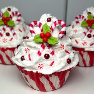 May include: Three festive cupcakes with white frosting, red and white striped candy canes, and red berry accents. The cupcakes sit in red and white striped paper cups, perfect for holiday celebrations.