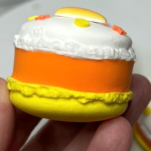 Puede incluir: Primer plano de una decoraci&oacute;n en forma de caramelo de ma&iacute;z. La decoraci&oacute;n tiene una parte superior blanca con chispas, un centro naranja y una parte inferior amarilla. Una peque&ntilde;a pieza amarilla y naranja est&aacute; en la parte superior.