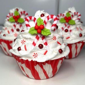 May include: Three festive cupcakes with white frosting, red and white striped wrappers, and candy cane decorations. Each cupcake is topped with a candy cane, holly leaves, and red berry accents, perfect for the holiday season.