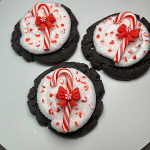 May include: Three chocolate cookies decorated with white frosting, red and white candy canes, and red bows. The cookies are on a white plate.
