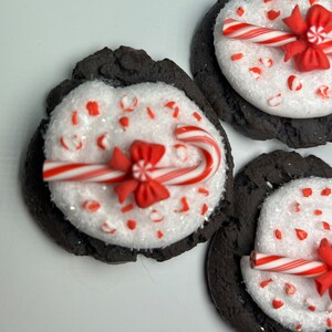 May include: Three chocolate cookies decorated with white frosting, red and white candy canes, and red bows. The cookies are on a white plate.