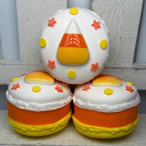 Puede incluir: Tres golosinas tem&aacute;ticas de Halloween que se asemejan a caramelos de ma&iacute;z. Cada golosina tiene una parte superior blanca decorada con estrellas naranjas y c&iacute;rculos amarillos. La base es naranja con un borde amarillo. La golosina superior presenta un dise&ntilde;o de caramelo de ma&iacute;z.