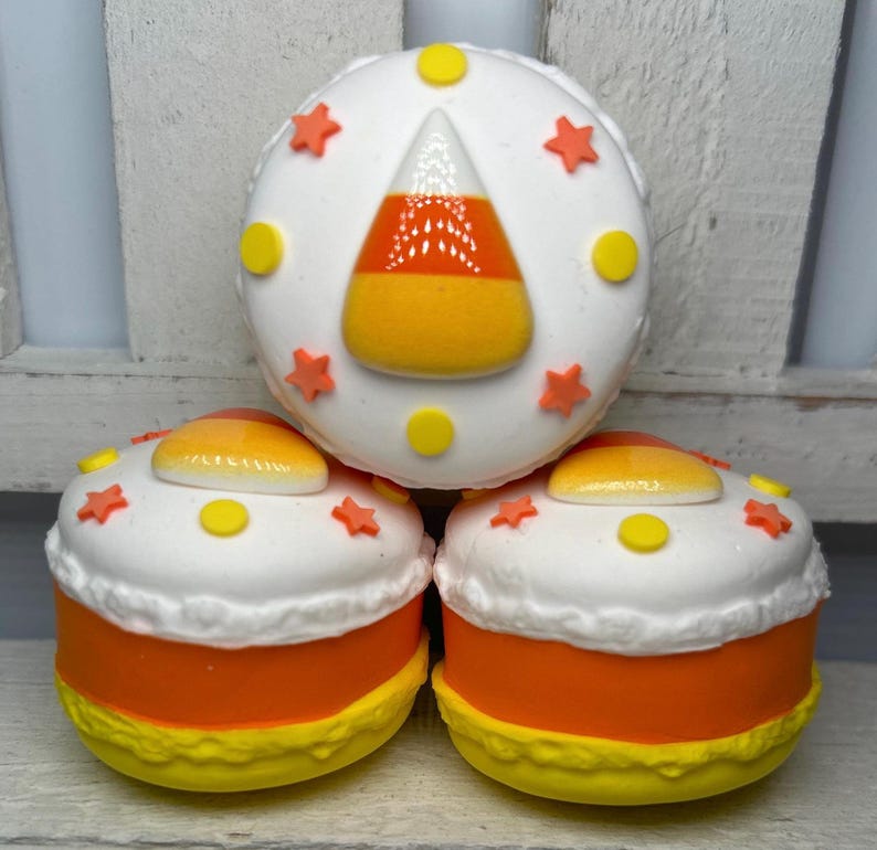 Puede incluir: Tres golosinas tem&aacute;ticas de Halloween que se asemejan a caramelos de ma&iacute;z. Cada golosina tiene una parte superior blanca decorada con estrellas naranjas y c&iacute;rculos amarillos. La base es naranja con un borde amarillo. La golosina superior presenta un dise&ntilde;o de caramelo de ma&iacute;z.