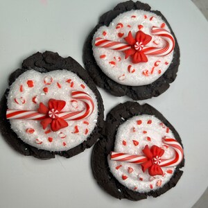 May include: Three chocolate cookies decorated with white sprinkles, red and white candy canes, and red bows.
