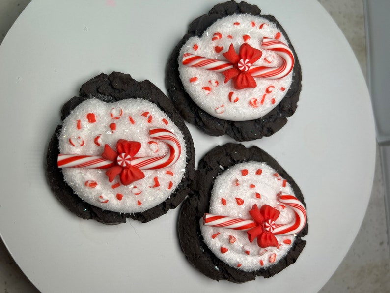 May include: Three chocolate cookies decorated with white sprinkles, red and white candy canes, and red bows.