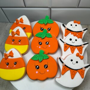 Pode incluir: Uma cole&ccedil;&atilde;o de nove biscoitos de a&ccedil;&uacute;car com tema de Halloween decorados com glac&ecirc; laranja, amarelo, branco e verde. Os biscoitos apresentam ab&oacute;boras, fantasmas e milho doce com carinhas fofas e la&ccedil;os.