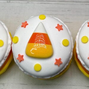 Puede incluir: Tres dulces redondos glaseados de blanco con dise&ntilde;os de caramelos de ma&iacute;z. Cada uno tiene un caramelo de ma&iacute;z en el centro, rodeado de estrellas naranjas y puntos amarillos. Los lados est&aacute;n en capas de amarillo y naranja.