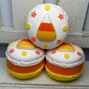 Puede incluir: Tres objetos redondos y decorativos que se asemejan a caramelos de ma&iacute;z. Cada uno tiene una parte superior blanca con estrellas naranjas y c&iacute;rculos amarillos. Los lados son naranjas y los fondos son amarillos. El objeto superior presenta un dise&ntilde;o de caramelo de ma&iacute;z.