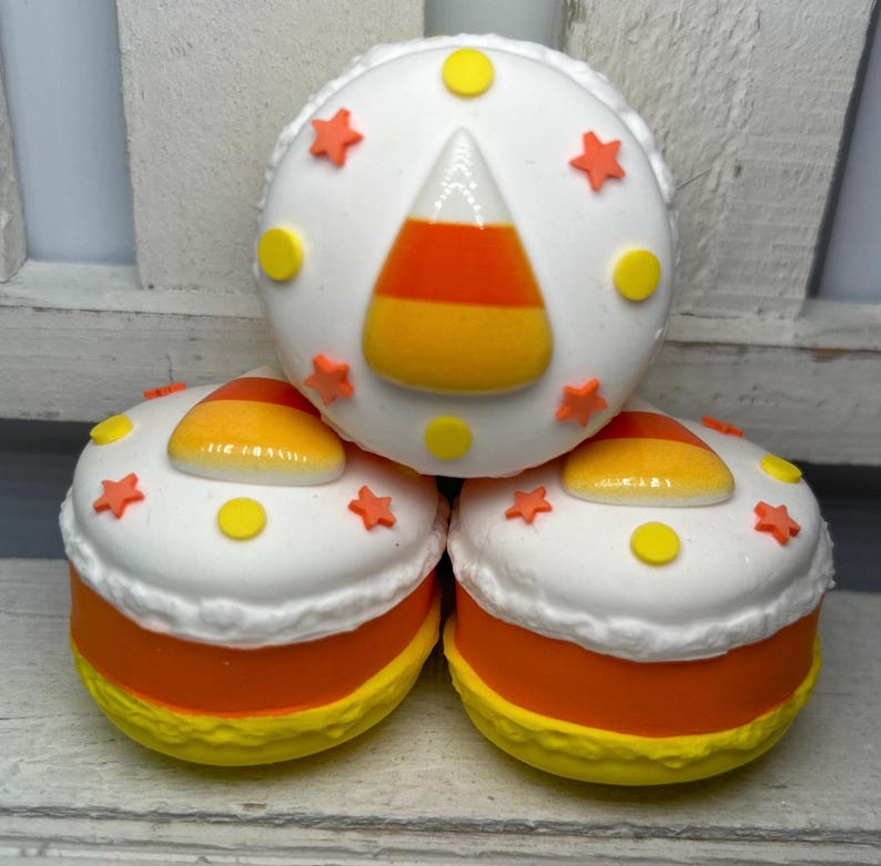 Puede incluir: Tres objetos redondos y decorativos que se asemejan a caramelos de ma&iacute;z. Cada uno tiene una parte superior blanca con estrellas naranjas y c&iacute;rculos amarillos. Los lados son naranjas y los fondos son amarillos. El objeto superior presenta un dise&ntilde;o de caramelo de ma&iacute;z.