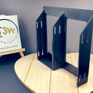 Puede incluir: Soporte de plástico negro impreso en 3D con múltiples ranuras y agujeros. El soporte está diseñado para sujetar un dispositivo u objeto.