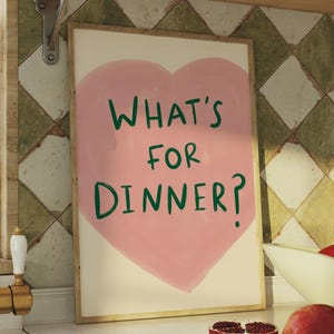 May include: A kitchen with a white countertop and a gold tap. A framed print with a pink heart and the text "What's for dinner?" is hanging on the wall. There are pomegranates on the counter and in a bowl.