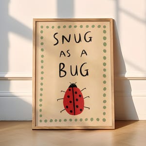 May include: A framed print with a beige background and green polka dots around the border. The print features a red ladybug with black spots and the text "Snug as a Bug" in black.