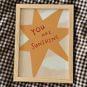May include: A framed print featuring a yellow star and the text "You are Sunshine" in red.