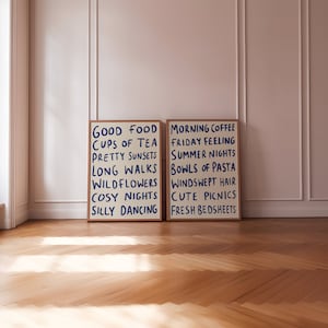 May include: Two framed prints with white backgrounds and blue text. The print on the left says "Good Food, Cups of Tea, Pretty Sunsets, Long Walks, Wildflowers, Cosy Nights, Silly Dancing". The print on the right says "Morning Coffee, Friday Feeling, Summer Nights, Bowls of Pasta, Windswept Hair, Cute Picnics, Fresh Bedsheets".