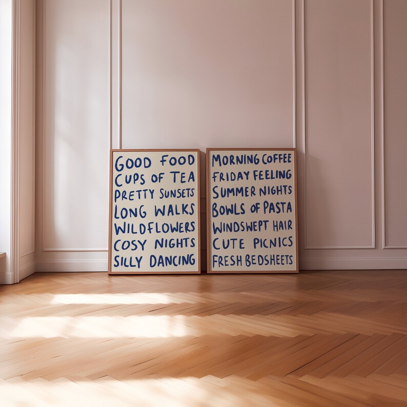 May include: Two framed prints with white backgrounds and blue text. The print on the left says "Good Food, Cups of Tea, Pretty Sunsets, Long Walks, Wildflowers, Cosy Nights, Silly Dancing". The print on the right says "Morning Coffee, Friday Feeling, Summer Nights, Bowls of Pasta, Windswept Hair, Cute Picnics, Fresh Bedsheets".