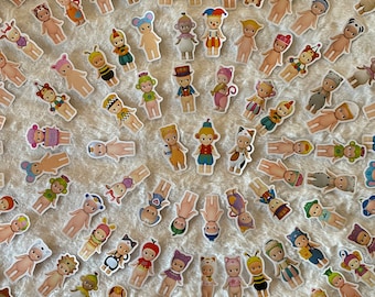 May include: A collection of colourful stickers featuring a variety of characters dressed in different costumes. The characters are all small, round, and have large eyes. The stickers are perfect for adding a touch of whimsy to any project.