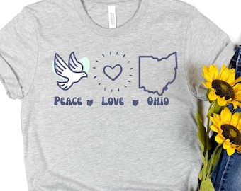 Könnte beinhalten: Graues T-Shirt mit einer Taube, einem Herzen und einem Umriss des Bundesstaates Ohio. Der Text "Peace Love Ohio" ist unter den Bildern gedruckt.