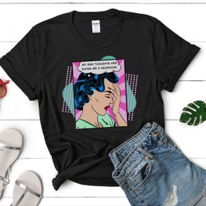 K&ouml;nnte beinhalten: Schwarzes T-Shirt mit einem Pop-Art-Grafikdruck einer Frau mit Kopfschmerzen. Die Grafik enth&auml;lt den Text "Meine eigenen Gedanken bereiten mir Kopfschmerzen."