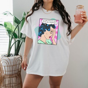 K&ouml;nnte beinhalten: Wei&szlig;es Oversize-T-Shirt mit einer Pop-Art-Grafik einer Frau mit Kopfschmerzen. Die Grafik sagt "Meine eigenen Gedanken bereiten mir Kopfschmerzen."