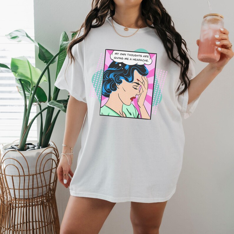 K&ouml;nnte beinhalten: Wei&szlig;es Oversize-T-Shirt mit einer Pop-Art-Grafik einer Frau mit Kopfschmerzen. Die Grafik sagt "Meine eigenen Gedanken bereiten mir Kopfschmerzen."