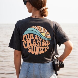 May include: A dark grey heather t-shirt with a graphic of a sun setting over a wave and the text "FOREVER CHASING SUNSETS".