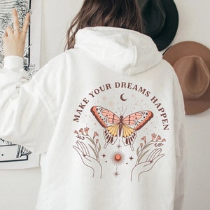 Könnte beinhalten: Weißer Hoodie mit einem Schmetterlingsmotiv und dem Text "Make your dreams happen".
