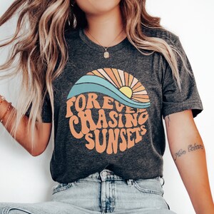 May include: Dark grey heather t-shirt with a graphic of a sun setting over a wave and the text "Forever Chasing Sunsets".