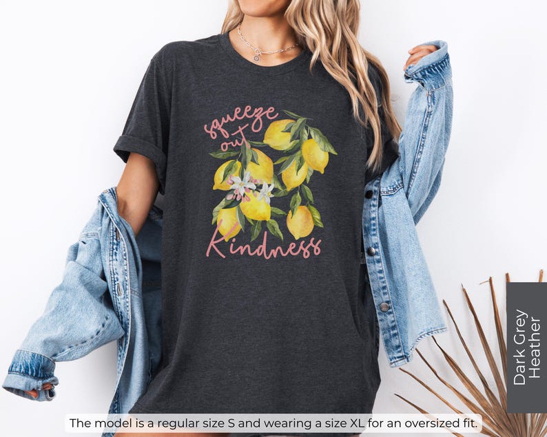 K&ouml;nnte beinhalten: Dunkelgraues T-Shirt aus Heather-Material mit einem Zitronenmotiv und dem Text "squeeze out kindness" in Rosa.