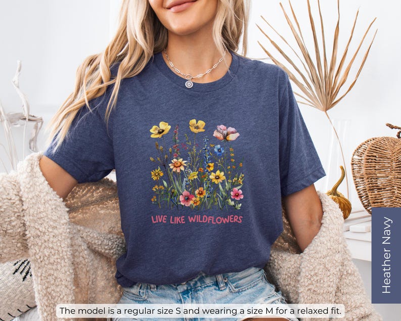Puede incluir: Una camiseta azul marino con un dise&ntilde;o floral y el texto "LIVE LIKE WILDFLOWERS".