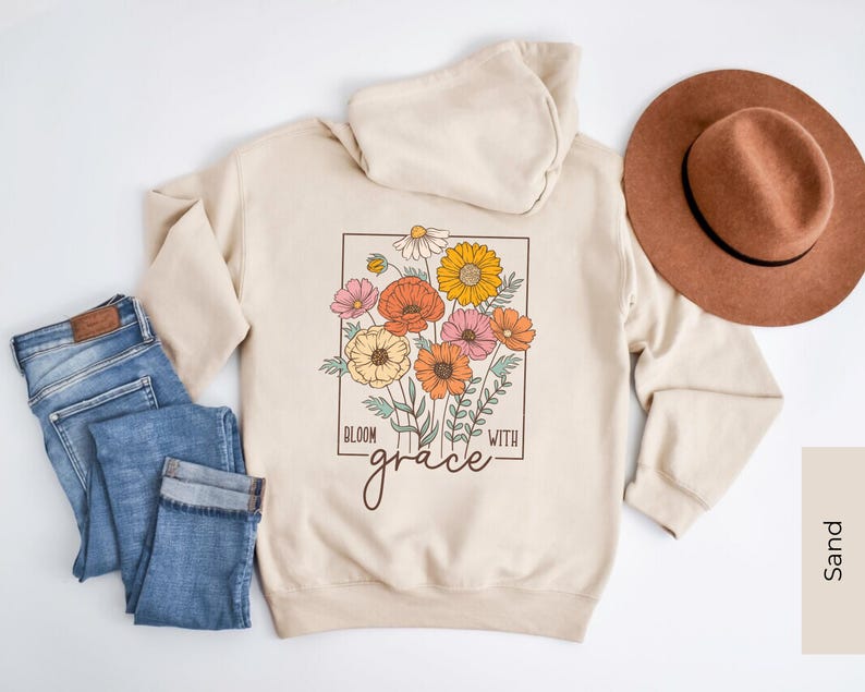 May include: A beige hoodie with a floral design and the text "Bloom with grace" on the front. The hoodie has a hood and long sleeves.