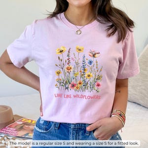 Puede incluir: Camiseta rosa con un dise&ntilde;o floral y el texto "Live Like Wildflowers".