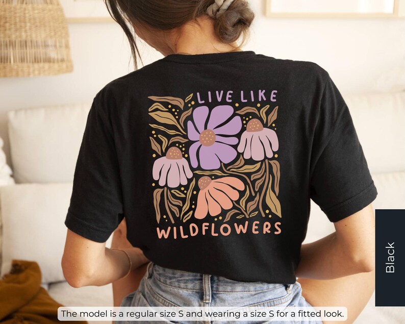 May include: Black t-shirt with a floral design featuring the text "LIVE LIKE WILDFLOWERS." The design includes purple, peach, and tan flowers with green leaves. The shirt is a regular size S and is worn for a fitted look.