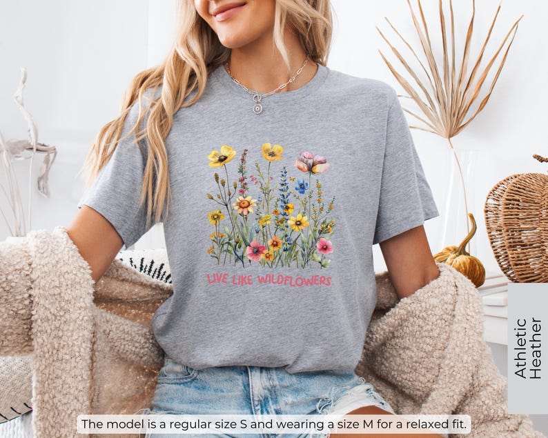 Puede incluir: Camiseta deportiva gris jaspeada con un dise&ntilde;o floral y el texto "Live Like Wildflowers".