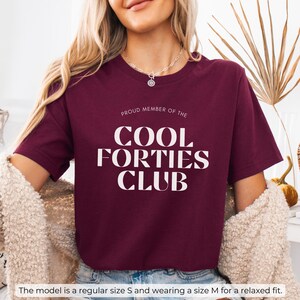 May include: A maroon t-shirt with white text that reads "Proud Member of the Cool Forties Club".