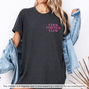 May include: A dark grey heather t-shirt with the text "COOL FORTIES CLUB" in pink lettering.