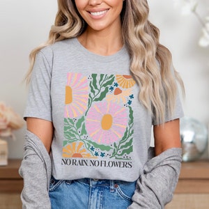 May include: A gray t-shirt with a floral design and the text "NO RAIN, NO FLOWERS" printed on the front. The shirt is made of a soft, comfortable material and is perfect for everyday wear.