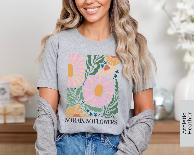 May include: A gray t-shirt with a floral design and the text "NO RAIN, NO FLOWERS" printed on the front. The shirt is made of a soft, comfortable material and is perfect for everyday wear.