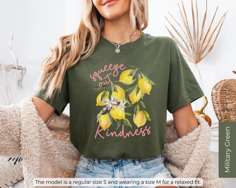 K&ouml;nnte beinhalten: Gr&uuml;nes T-Shirt mit einem Zitronenmotiv und dem Text "squeeze out kindness" in rosa Schrift.