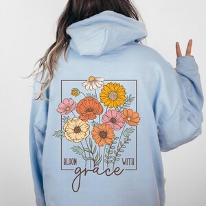 May include: Light blue hoodie with a floral design and the text "Bloom with grace" on the back.