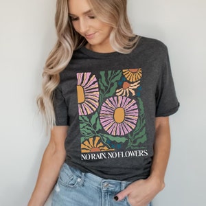 May include: A dark grey heather t-shirt with a floral design and the text "NO RAIN NO FLOWERS".