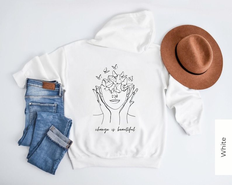 May include: White hooded sweatshirt with a black line drawing of a person with butterflies around their head. The text "change is beautiful" is printed below the drawing.