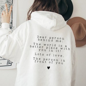 May include: White hoodie with a black text message on the back that reads: "Dear person behind me: The world is a better place with you in it! Lots of love, The person in front of you".