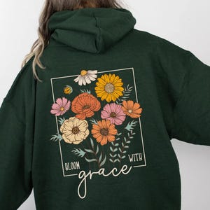 May include: Forest green hooded sweatshirt with a floral design and the text "Bloom with grace" printed on the back.