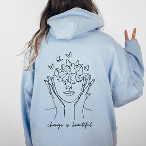 May include: Light blue hoodie with a black line drawing of a face with butterflies around it. The text "change is beautiful" is printed below the drawing.
