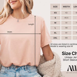 May include: A light peach-colored Unisex Jersey Short Sleeve Tee is shown with a size chart. The chart lists sizes XS to 2XL, with measurements in centimeters. The model is wearing size M. The brand name is Abby Moon Apparel.